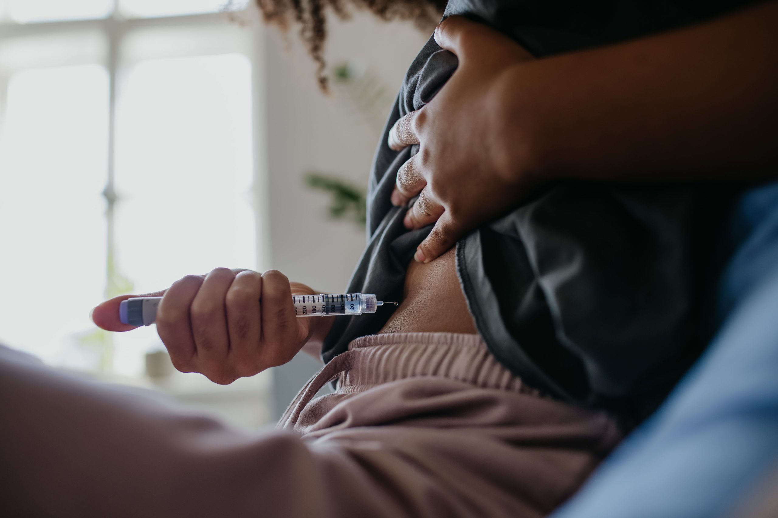 dark-skinned person holding syringe to exposed stomach area for injection